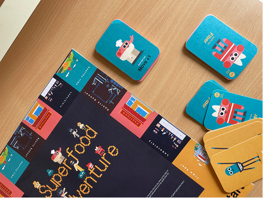 Close view of the printed board with cut-out standees and card decks resting on it.